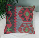 Kelimkissen mit graphischem Muster in rot-gruen-schwarz Toenen auf weisem Sofa